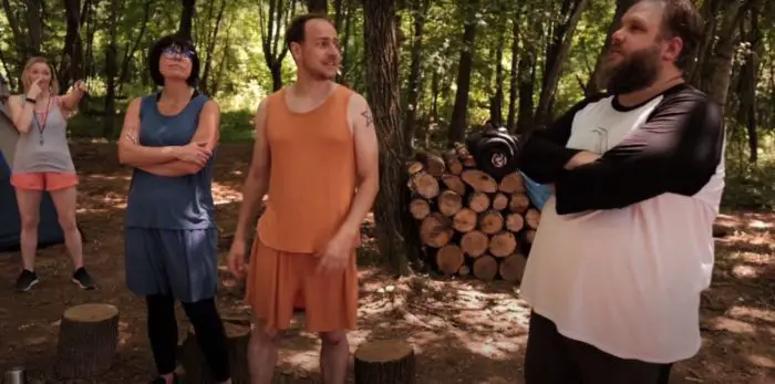 Sarah, Linda, Larry, and Matt stand in frond of a cord of wood at a campsite in All Your Friends Are Dead