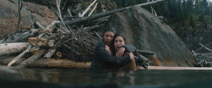 Carmen and Joy hold each other waist deep in water next to a dam in Dark Nature