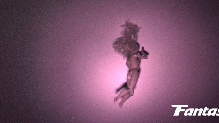 A naked doll hangs from the ceiling as a flashlight shines on it in Skinamarink