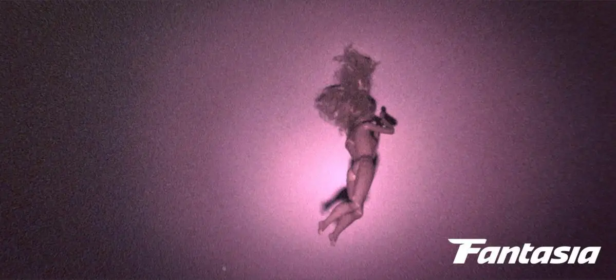 A naked doll hangs from the ceiling as a flashlight shines on it in Skinamarink