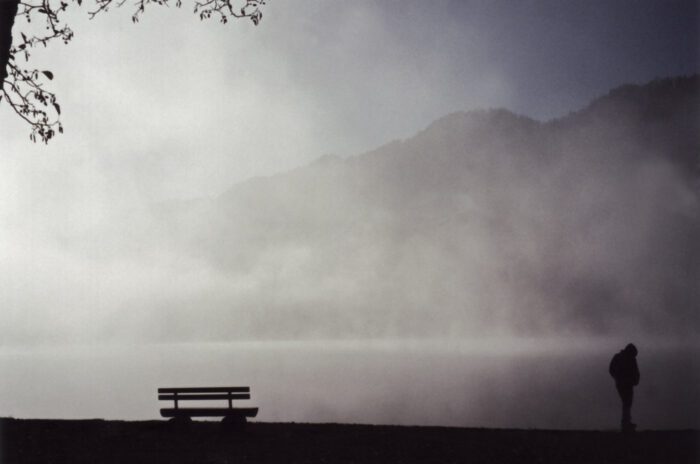 An expression of loneliness - a foggy area with one single bench and the silhouette of a man in the corner