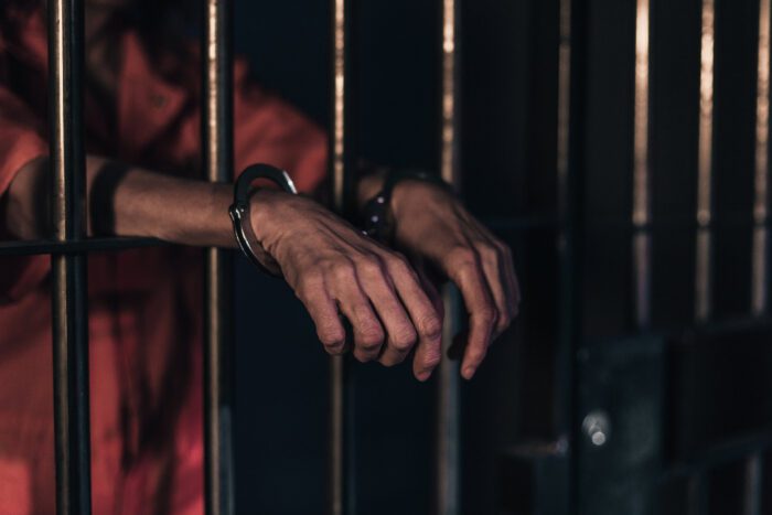 A prisoner wearing handcuffs, locked behind bars