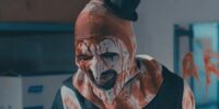 Art the clown stands smiling covered in blood in the Terrifier 2 trailer