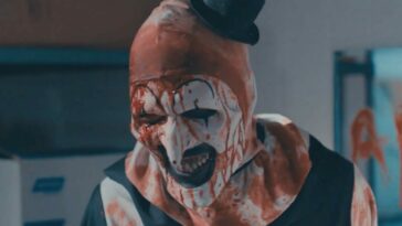 Art the clown stands smiling covered in blood in the Terrifier 2 trailer