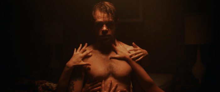 Eli is shown shirtless in low light with hands all over him in What Josiah Saw