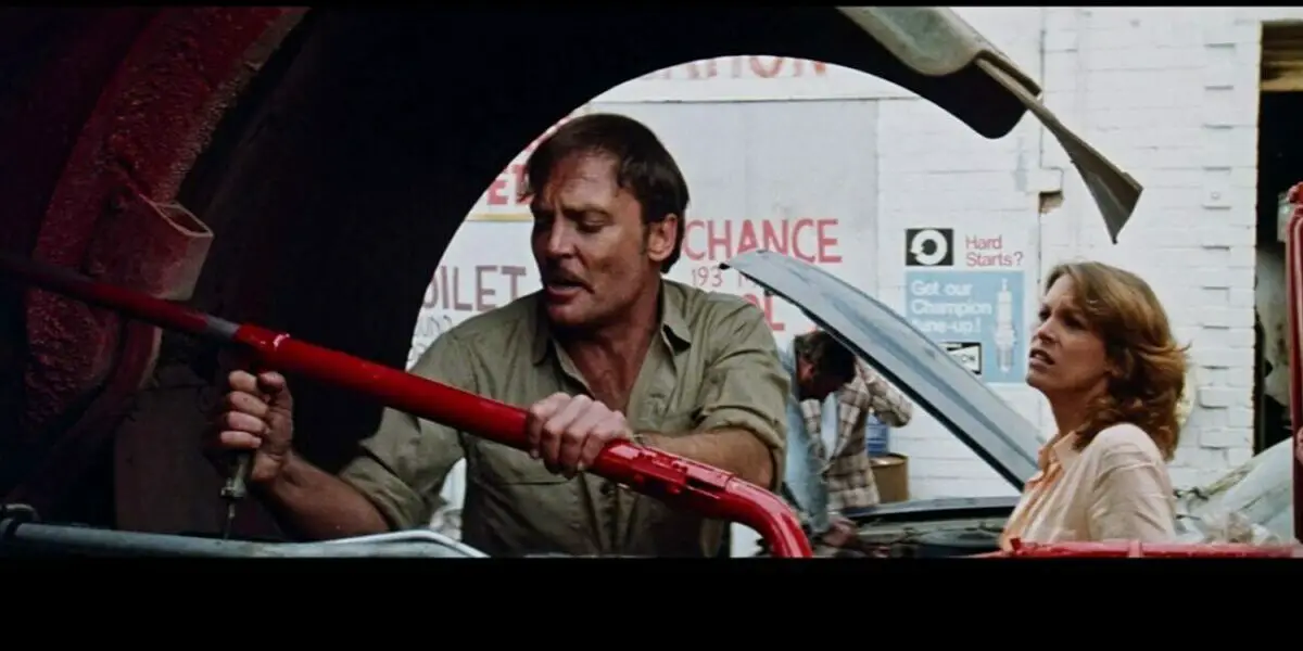 Quid (Stacey Keach) tends to his rig while conversing with the young hitchhiker "Hitch" (Jamie Lee Curtis)