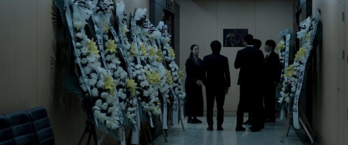 A group of people speak to Ye-young in a funeral home hall lined with flower displays in Seire