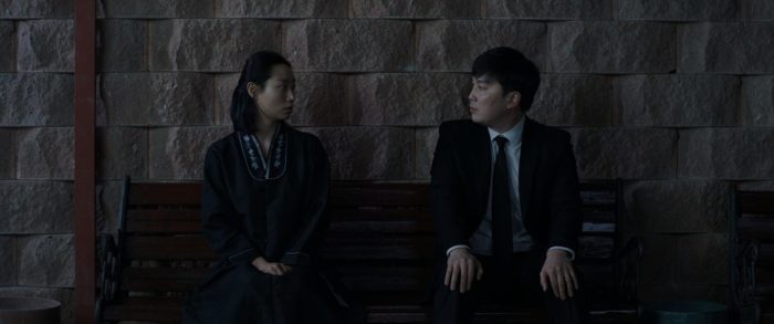 Ye-young and Woo-jin sit looking at one another on a bench in Seire