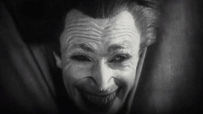 Gwynplaine with his frozen grin stares out through a stage curtain in The Man Who Laughs