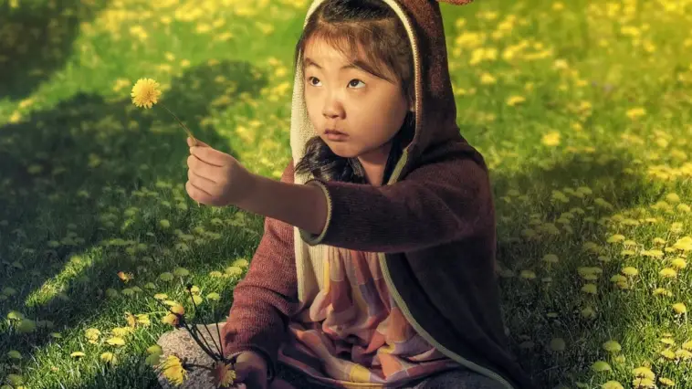 A young Asian girl holds up a dandelion to a person off screen