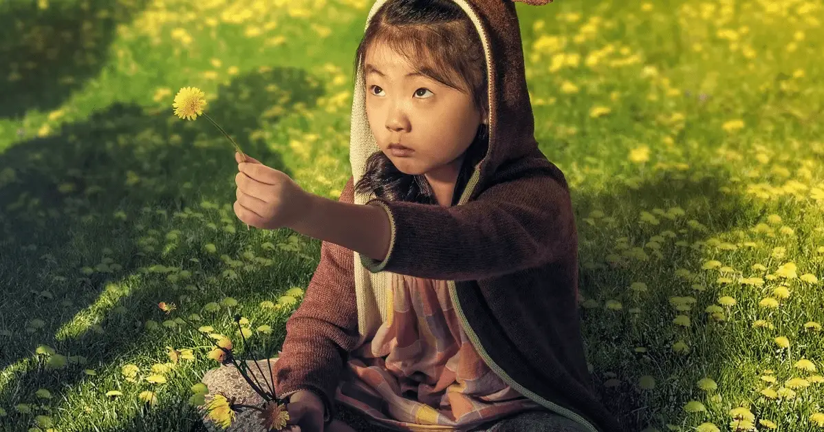 A young Asian girl holds up a dandelion to a person off screen