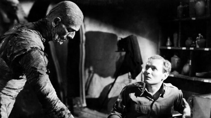 The Mummy leans across a table as a terrified man stares at the monster.