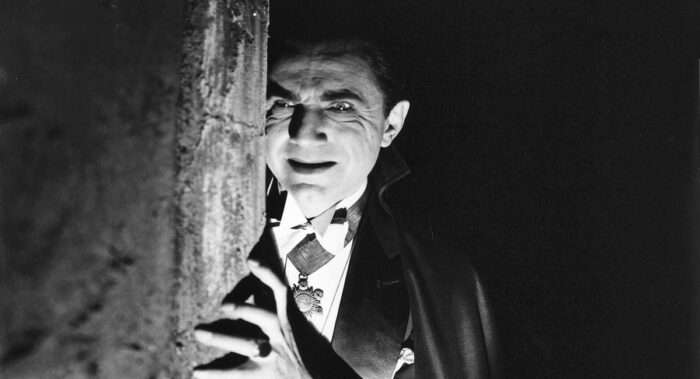 Bella Lugosi's Dracula leers around the corner of a pillar in his crypt, his face contorted and lit from below.