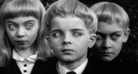 David, the main protaganist in Village of the Damned, flanked by two other children stare out at you, with their eyes glowing.