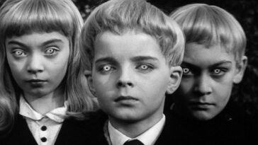 David, the main protaganist in Village of the Damned, flanked by two other children stare out at you, with their eyes glowing.