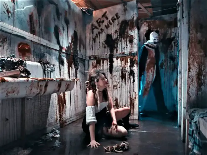 Art the Clown approaches his next victim, a young lady on the floor in a blood drenched bathroom. 
