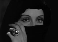 Countess Marya Zaleska (Gloria Holden) stares intensely while holding a cloth over the lower half of her face, wearing a ring with a large jewel on it, in the film, "Dracula's Daughter" (1936).