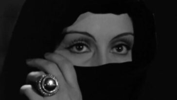 Countess Marya Zaleska (Gloria Holden) stares intensely while holding a cloth over the lower half of her face, wearing a ring with a large jewel on it, in the film, "Dracula's Daughter" (1936).