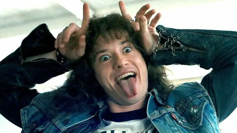 Eddie Munson from Stranger Things wears a Hellfire Club T-shirt and uses fingers to make devil horns on his head.