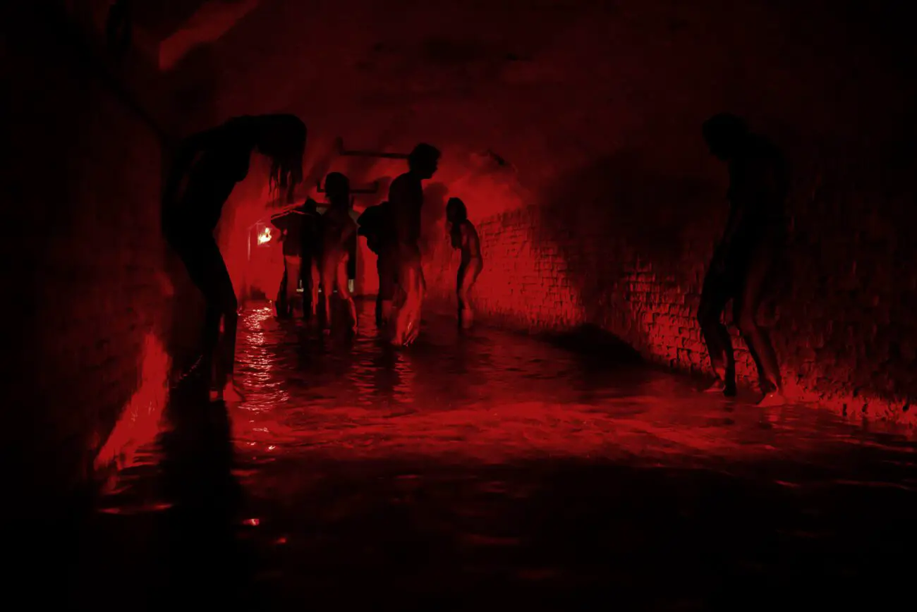 Multiple people stand in a red-lit sewer tunnel