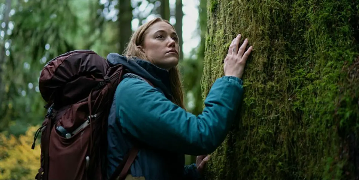 Ruth is seen with her backpack on with her right hand on a tree in Significant Other