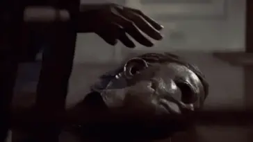 A hand reaching for the iconic Michael Myers mask