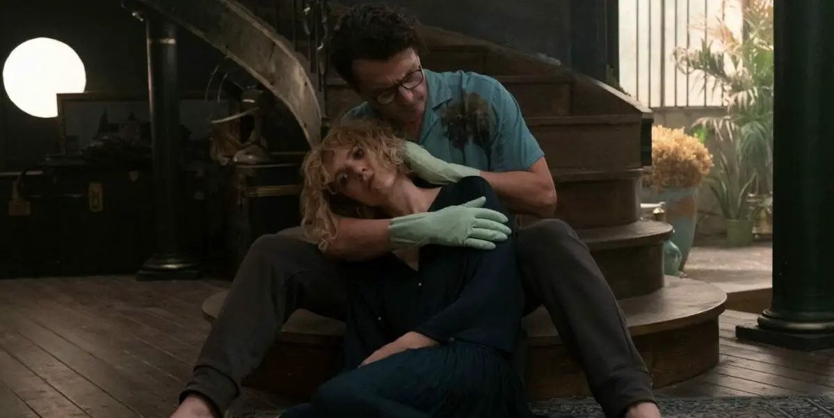 The Guest holds an unconscious Stella at the base of a staircase in The Guest Room