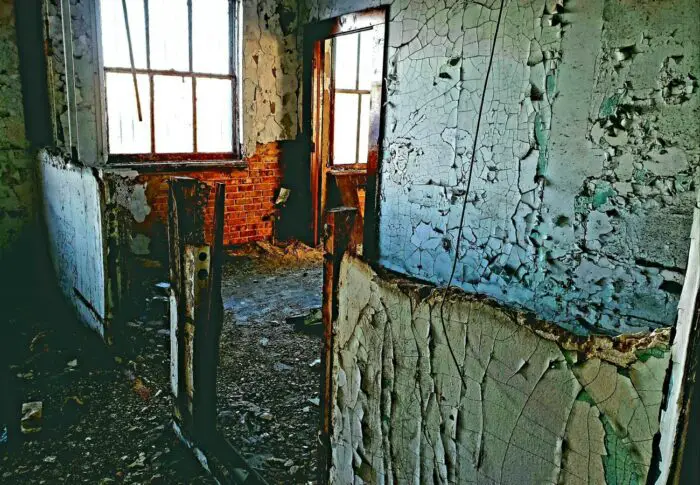 Decaying room in an abandoned building. Cracked peeling plaster and paint on all the walls, crumbling debris everywhere.