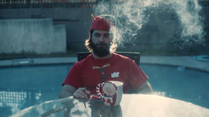 Dylan sits smoking poolside in festive attire in Breathing Happy