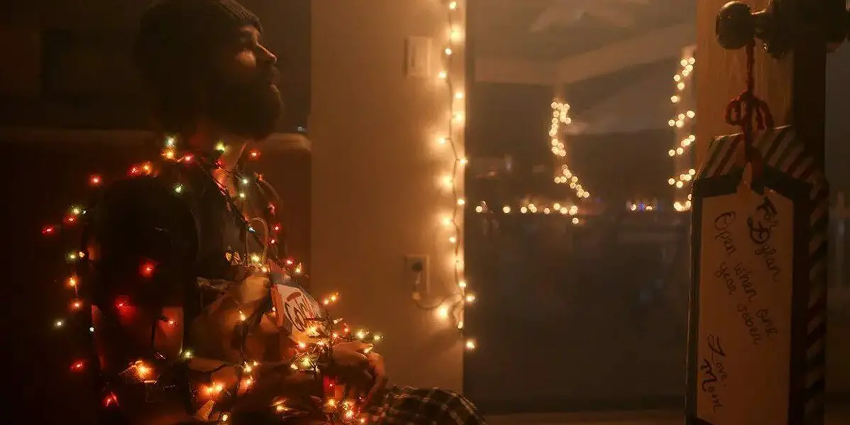 Dylan sits in a chair tied up by Christmas lights in front of a door with a gift tag on it in Breathing Happy