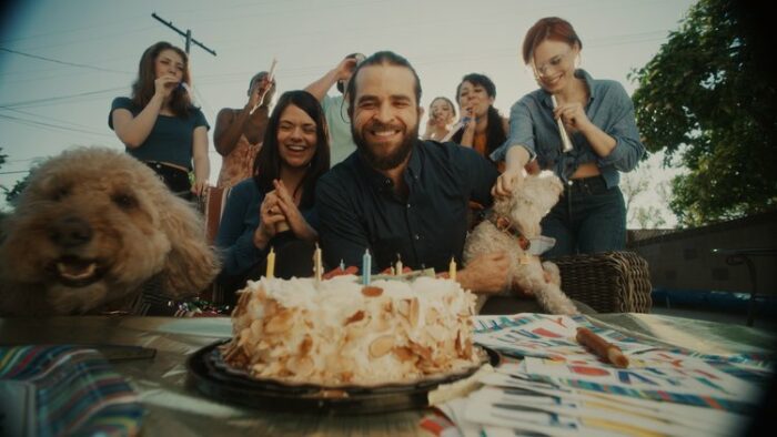 Dylan's family surround him outdoors by a table with a cake on it.