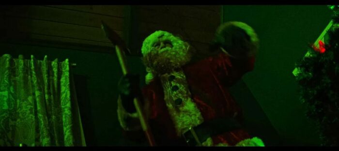 Santa Claus standing in a green light has an ax in his hand and blood on his suit in Christmas Bloody Christmas.