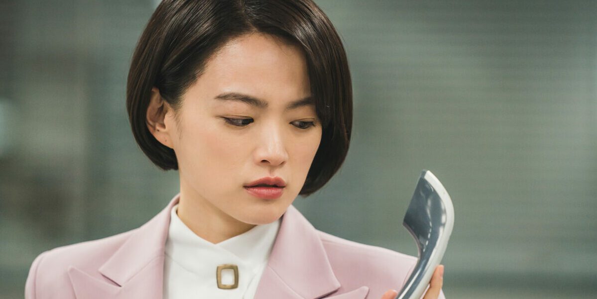 Se-Ra looks puzzled at a desk phone's receiver in The Anchor