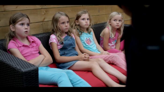 four young girls sit on a wicker loveseat