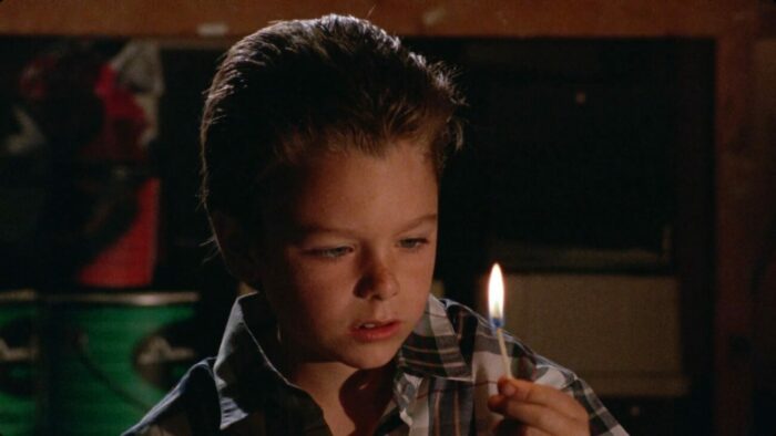 A boy stares at the lit match he's holding