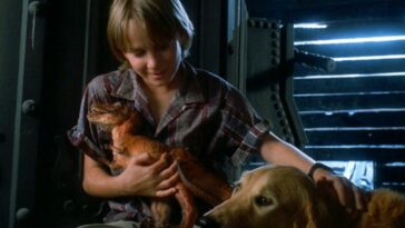 A boy sitts cuddling a baby T-Rex and petting his dog in Prehysteria!