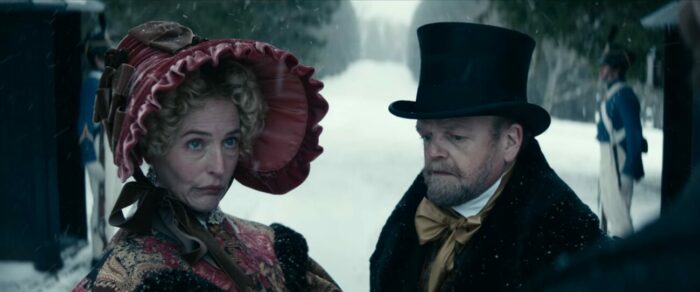 Gillian Anderson sports a bonnet and Toby Jones, a top hat, standing in a snow covered path in The Pale Blue Eye