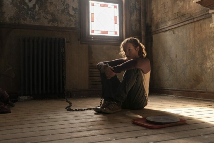 Ellie sits on the floor, chained to a radiator in a room devoid of furniture in The Last of Us episode 1 "When You’re Lost in the Darkness.”