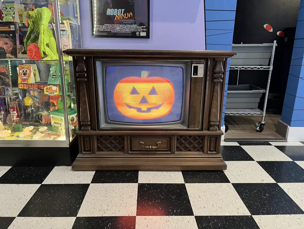 A TV shows a flickering jack-o-lantern cartoon image in the coffee shop, "The Brewed."