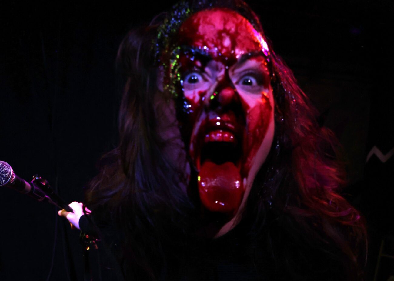 Maria stares down the audience, face covered in blood and her tongue sticking out