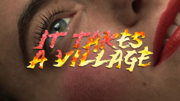 Title card for it Takes A Village, flame filled text spells "It takes a village" overlayed on top of the face of a woman