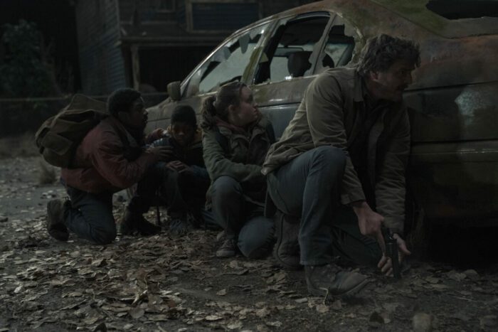 (L-R) Henry, Sam, Ellie, and Joel hide behind a car that has all the windows shattered in The Last of Us S1E5 "Endure and Survive"