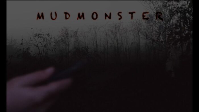 Title card for Mudmonster, black text spells "Mudmonster" on the top third of the screen, overlayed over an image of the woods