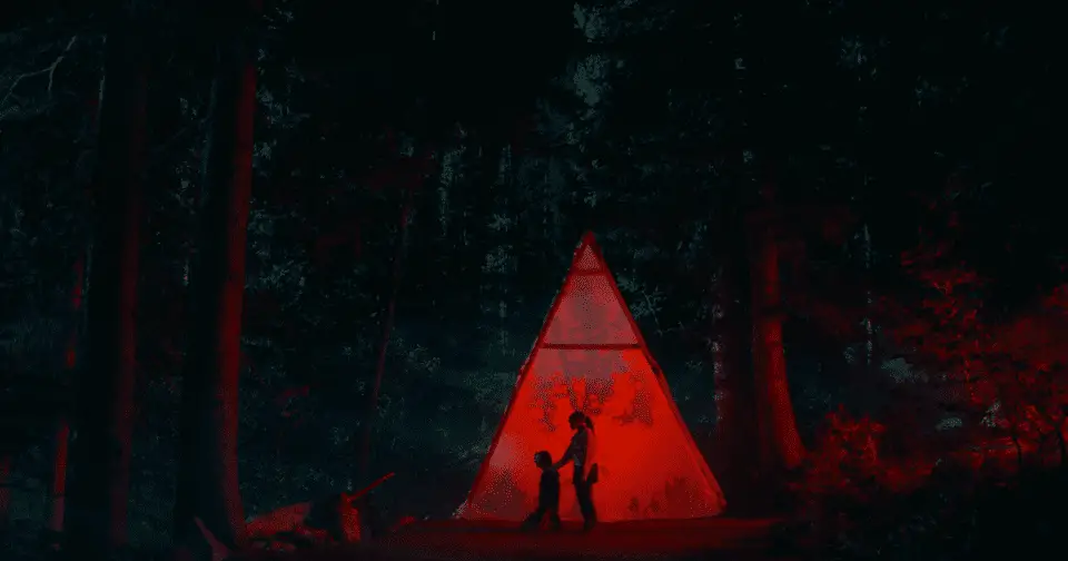Malcolm kneels in front of the red tent, while Emma stands behind him with her hand on his shoulder