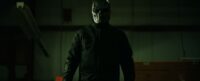 A masked assailant stands with an intimidating figure.