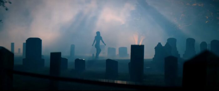 The silhouette of a woman walks through a foggy graveyard in Kill Her Goats