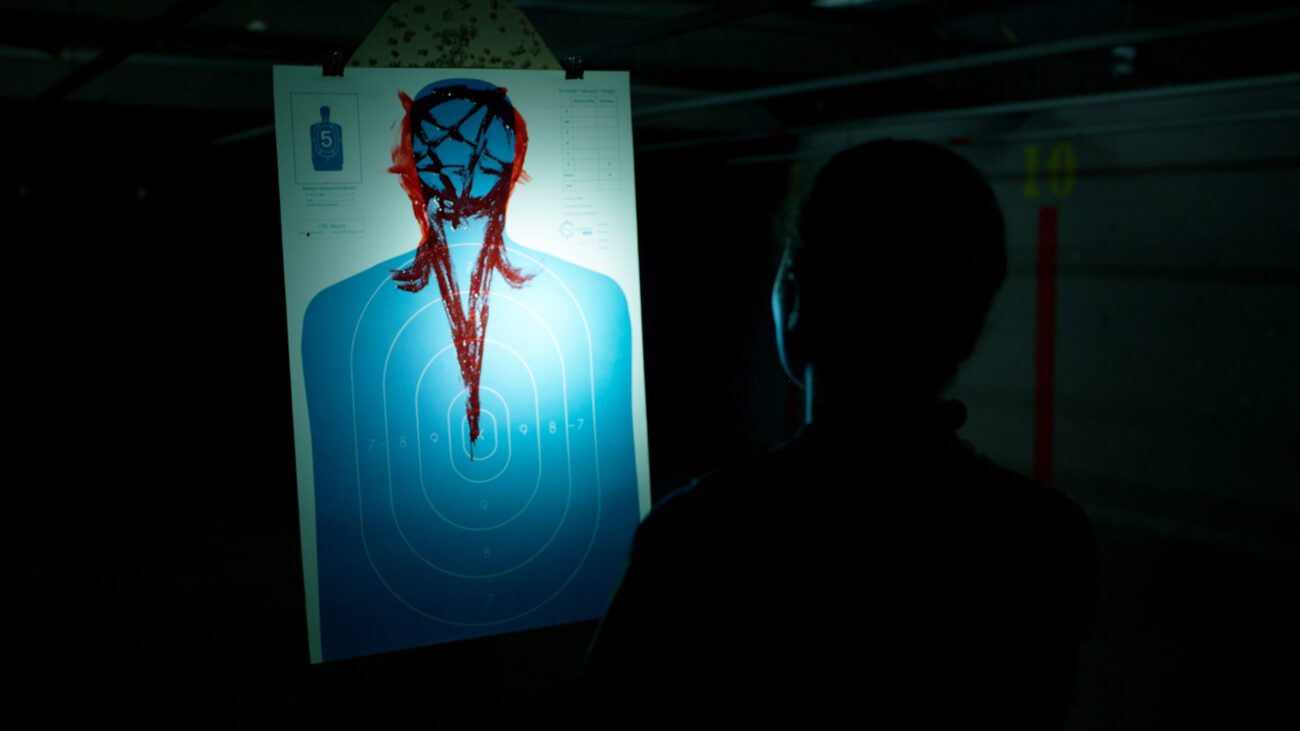 Jessica stands at the end of a dark shooting range as a target approaches her with a bloody pentagram where the head is