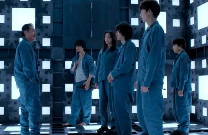 Everyone stands in a cube lit by white lights