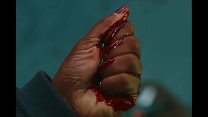 Dre squeezes a shard of glass in her hand, causing blood to spill out over her palm