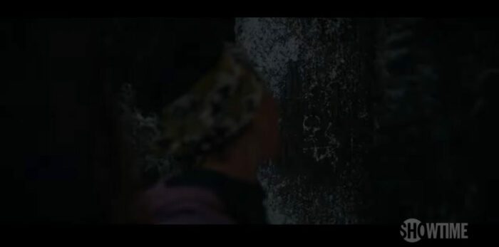 Taissa looks at the symbol carved in a tree